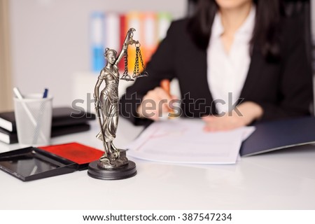 Statuette of Themis - the goddess of justice on lawyer's desk. Lawyer is stamping the document. Law office concept.  Royalty-Free Stock Photo #387547234
