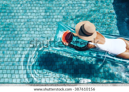 Girl floating on beach mattress and eating watermelon in the blue pool. Tropical fruit diet. Summer holiday idyllic. Top view. Royalty-Free Stock Photo #387610156