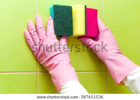 Hands in pink protective gloves cleaning tiles with colorful sponges. Early spring cleaning or regular clean up. Maid cleans house.