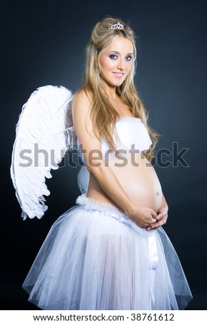 Beautiful young pregnant girl with angel wings standing on black background