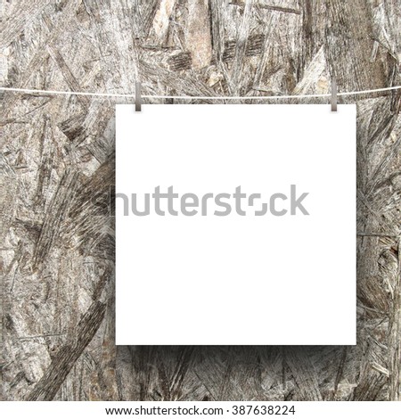 Close-up of one hanged square paper sheet frame with pegs on brown wooden background