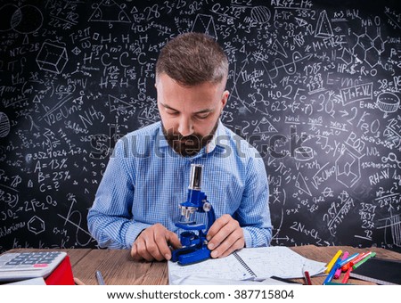 Hipster teacher at the desk with microscope, big blackboard