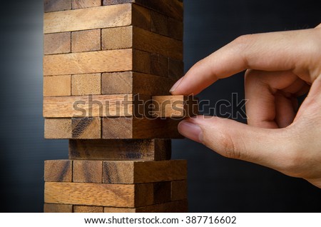 Closeup hand man take one block on The tower from wooden blocks, dark tone. Royalty-Free Stock Photo #387716602