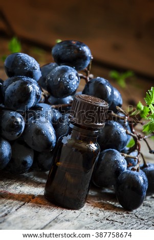 Grape seed oil in brown bottle, bunch of grapes, vine at the old wooden background, selective focus