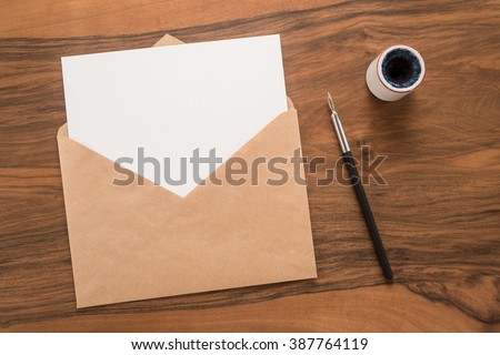 Envelope, ink pen, inkwell on a wooden background 
