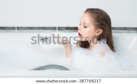 little girl playing with water and foam in bath.