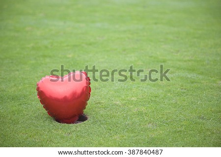 A red blown up heart on a golf green in bright weather on the left of the frame.