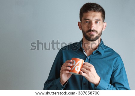Young business man wearing blue shirt, drinking coffee / tea in orange mug with percent sign