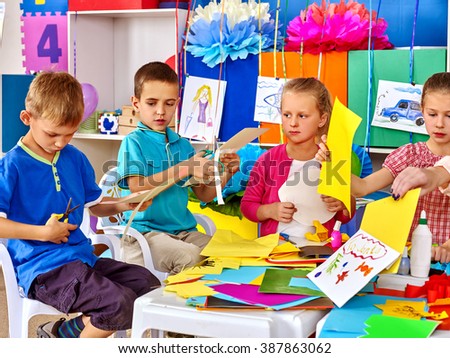 Group kids make applique of colored paper on table in kindergarten .