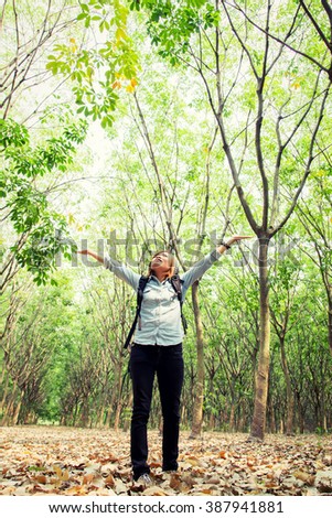 Beautiful young woman carrying backpack walking in forest raising her hands happy with fresh air