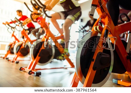 Young people working out on an exercise bike in gym, close-up Royalty-Free Stock Photo #387961564