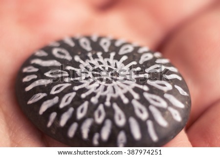 Macro close-up image of hand painted sea pebble. Mandala on hands. Relax, yoga, hinduism, ethno background. Shallow depth of field. Retro toned photo. Royalty-Free Stock Photo #387974251
