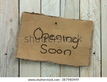 Cardboard sign on a wooden background saying opening soon