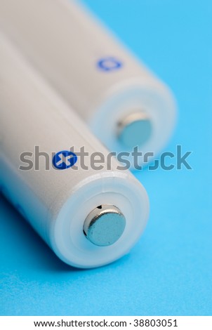 Macro shot of some two AA white electric batteries withour labels side by side on blue background