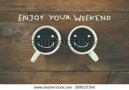coffee cup with happy faces next to "enjoy your weekend" phrase background. vintage filtered. happy weekend concept Royalty-Free Stock Photo #388033366