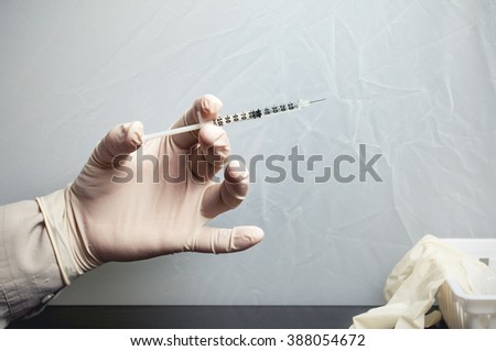 Rubber gloved hand holding a 1 ml syringe containing serum for injection.