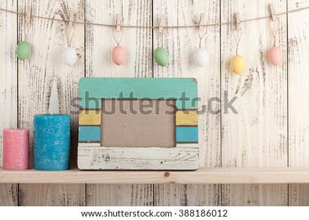 Easter eggs, blank frame and candles on wooden background