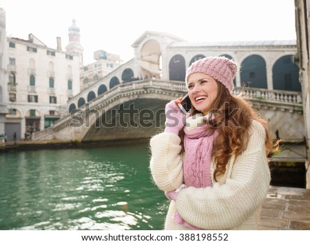 Ultimate getaway shortcut - start New Year going on Carnival in Venice, Italy. Happy young woman tourist in white sweater talking cell phone in the front of Rialto Bridge