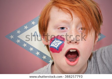 redhead fan boy with arkansas state flag painted on his face. 