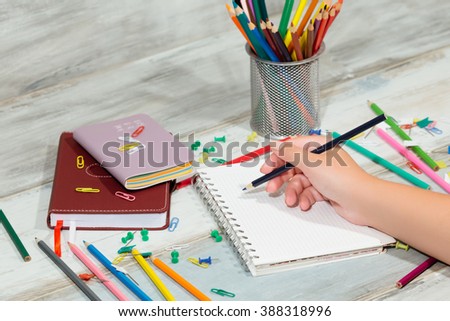 Woman's hand drawing writing in a notebook bright color pencils stationery on old wooden table vintage background