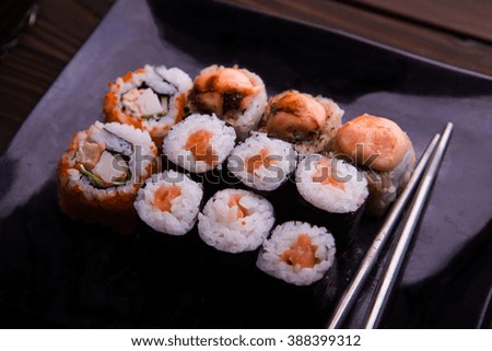 Assortments of sushi on black rectangle plate on rustic dark brown wooden background
