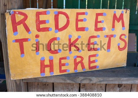 Handmade sign reading "Redeem Tickets Here" sits at booth of carnival.
