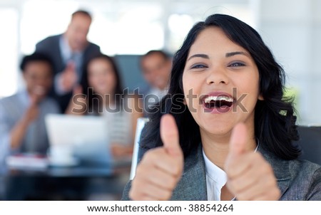 Happy businesswoman with thumbs up in office with her team in the background