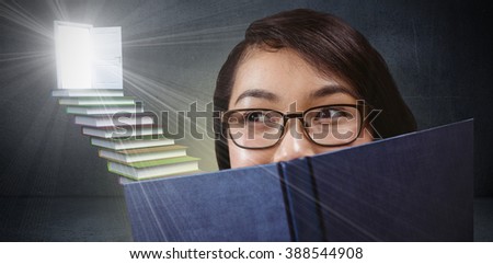 Pretty student hiding face behind a book against steps made from books leading to door in grey room