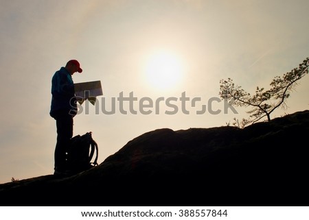 Silhouette of young tourist guide looking in paper  map in nature while hiking