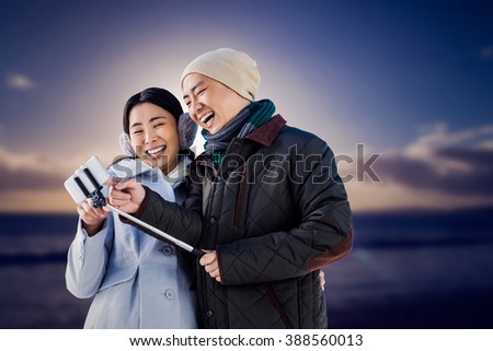Couple laughing at their pictures taken on smartphone against scenic view of sea against sky