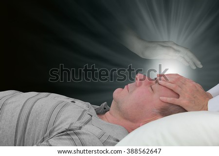 Channeling healing with a spirit guide - female hands laid on a male patient's forehead with an ethereal ghostly spirit hand hovering above and a glow of healing light  energy on a dark background Royalty-Free Stock Photo #388562647