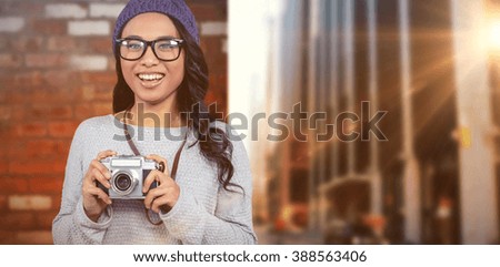 Asian woman holding digital camera against wall of a house