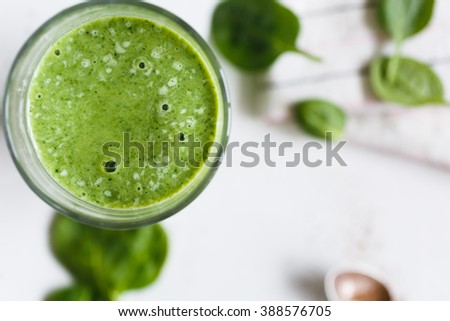 Green smoothie with banana and spinach, fresh herbs on the background, top view
