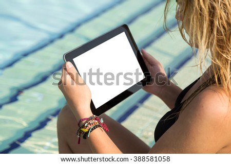 Beautiful blond sitting by the pool and surfing the web on her tablet computer