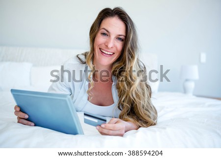 smiling woman lying on her bed on her tablet, holding her credit card
