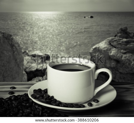Coffee beans and coffee in white cup on wooden table opposite a defocused natural landscape for background. Collage. Selective focus. Toned.