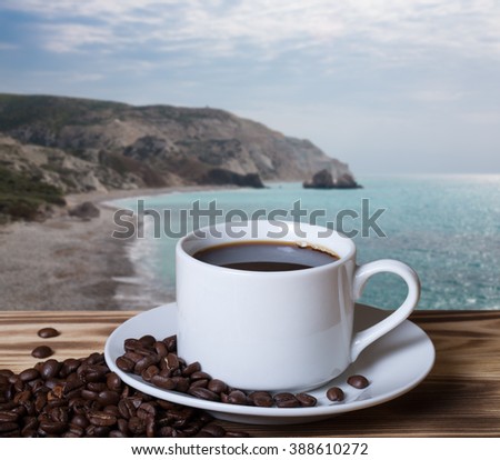 Coffee beans and coffee in white cup on wooden table opposite a defocused natural landscape for background. Collage. Selective focus.