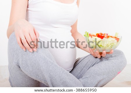 Beautiful young pregnant woman / teenager in white cloth eating healthy fresh salad with vegetebles