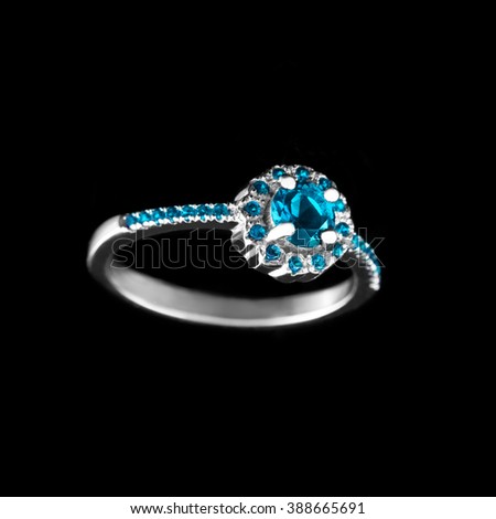 Luxury jewelry. White gold or silver engagement ring with colored gemstone closeup on black background. Selective focus