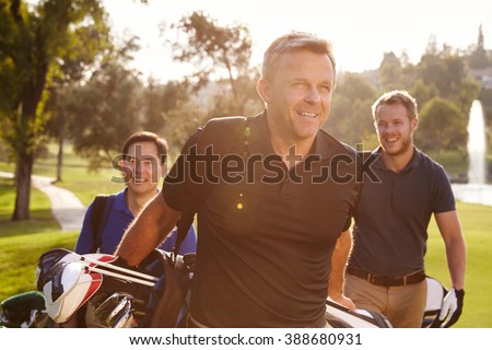 Group Of Male Golfers Walking Along Fairway Carrying Bags Royalty-Free Stock Photo #388680931