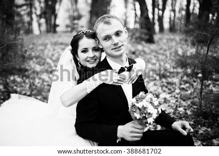 Happy wedding couple sitting at autumn forest with fell leaves from the trees