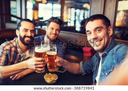 people, leisure, friendship, technology and bachelor party concept - happy male friends taking selfie and drinking beer at bar or pub