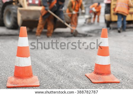 road workers repair the road,  cones in  foreground Royalty-Free Stock Photo #388782787