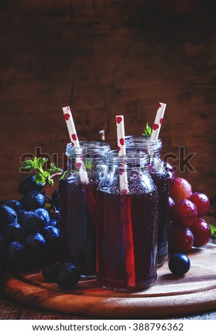 Dark grape juice in glass bottles with straws, blue grapes, dark toned image, selective focus
