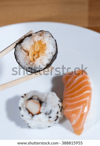 Eating sushi. Image taken against a wooden table with holding the food in chopsticks. 