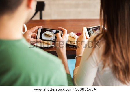 Point of view of a young couple taking photos of some slices of pie they just ordered for dessert with their smartphones