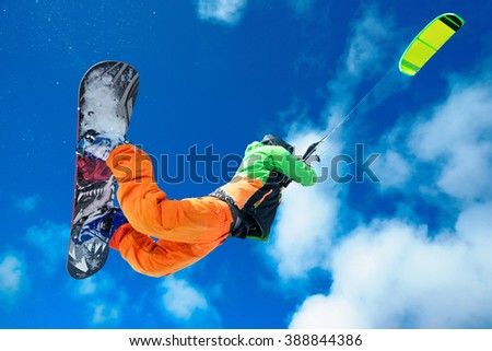 Male Athlete rides in the winter snowboarding and controls the kite. A clear winter day with clouds. Performs stunts and jumps Royalty-Free Stock Photo #388844386