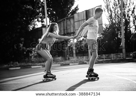 Beautiful sweet couple riding on roller skates holding hands on the street during sunset. Black and white
