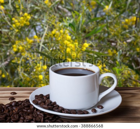 Coffee beans and coffee in white cup on wooden table opposite a defocused blossom background. Collage. Selective Focus.