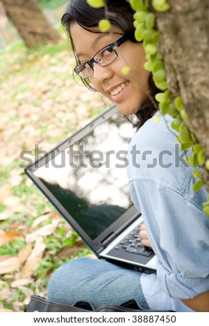 Asian female college student working on a laptop under a tree